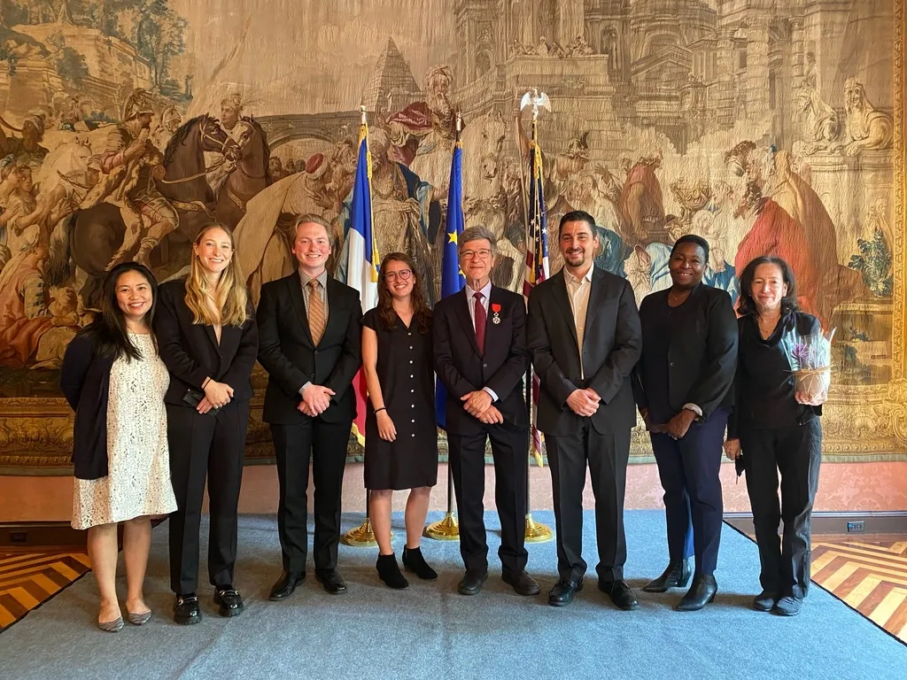 Eight people stand in a row in front of three flags