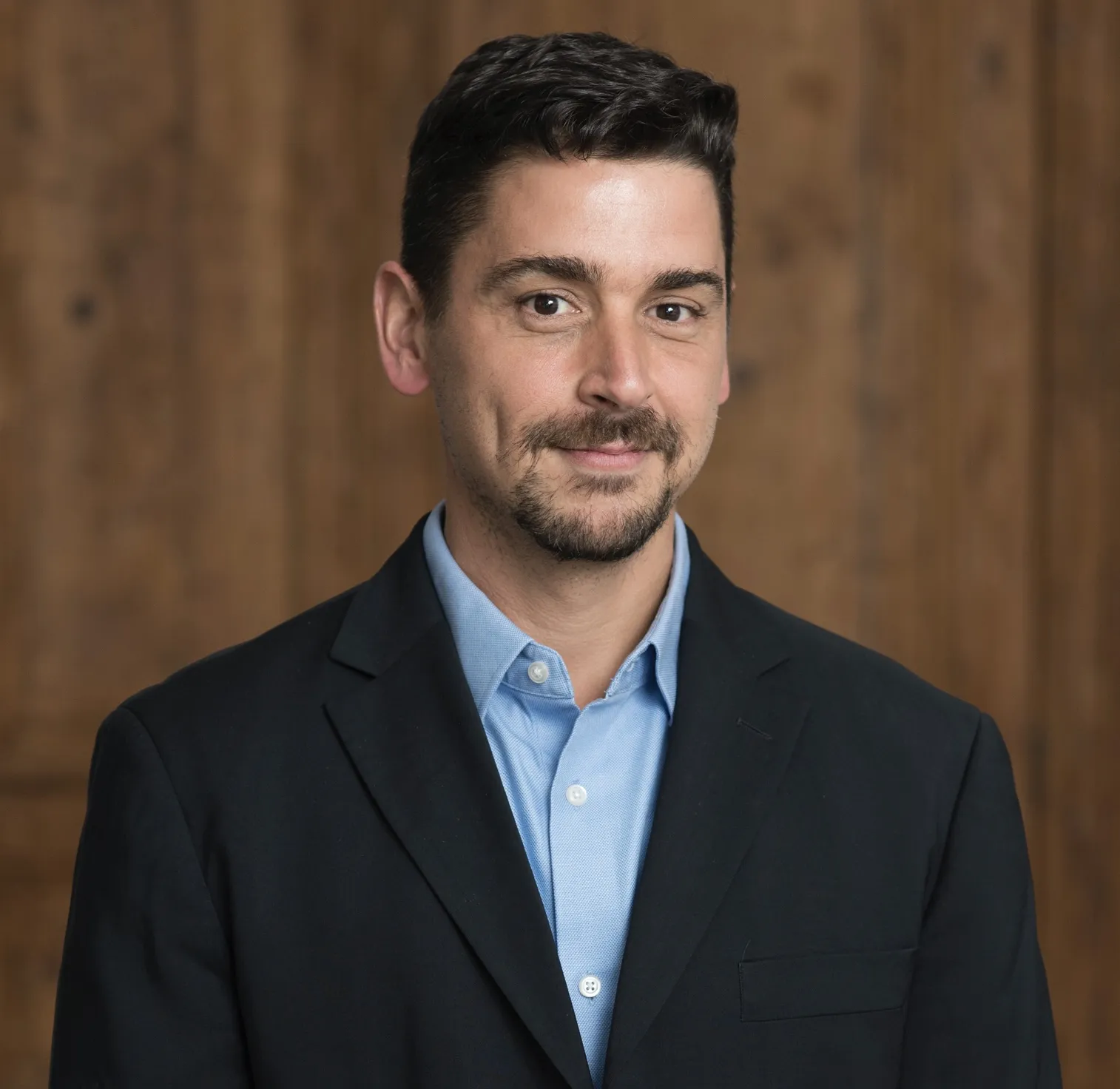 Man in suit with blue shirt on brown background.