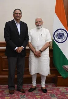 Two men stand next to a flag that is orange, green, and white.