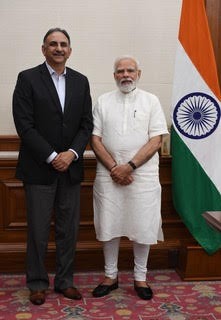 Two men stand next to a flag that is orange, green, and white.